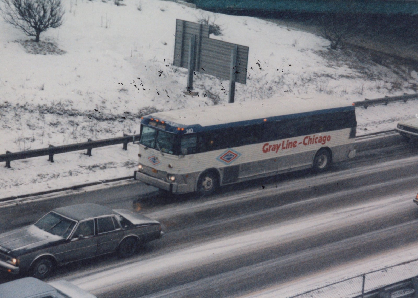 A white and blue Gray Line bus with the number 240 is driving on a snowy highway alongside other cars.