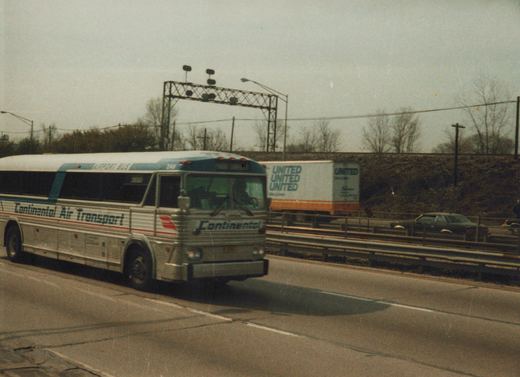 A white and blue Continental Air Transport bus drives on a highway with a truck and car in the background, under an overcast sky in winter.