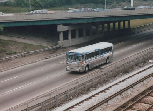 A silver and blue Continental Air Transport bus, number 106, drives on a highway median beside railroad tracks, with a concrete overpass carrying cars overhead; the bus's front sign reads 'O'Hare Airport'.