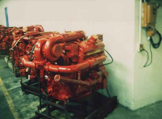 A close-up view of large, red industrial diesel engines mounted on black metal racks, lined up against a white cinder block wall inside a shop.