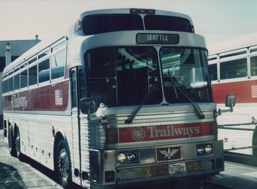 Front three-quarter view of a silver and red Trailways bus with 'SEATTLE' on the destination sign, showing multiple state license plates.