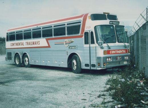 A side-front view of a large, silver and red Continental Trailways bus parked next to a chain-link fence in an unpaved lot.