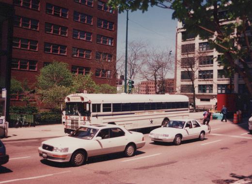 A white Cook County Sheriff's bus numbered 302, a Pullman 818A model, is parked or moving slowly on a city street with two white sedans in the foreground and pedestrians nearby.