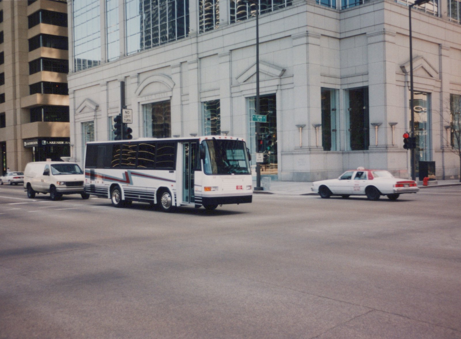 A white Pace bus with the number 33 drives on a city street at an intersection, with a white taxi cab and a white delivery van also present. A modern building with large windows is in the background.