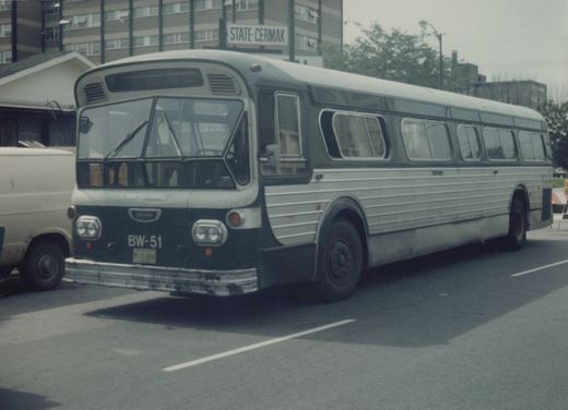 A vintage motor bus with a green and silver livery and the number BW-51 on its front, parked on an urban street with a sign reading 'STATE-CERMAK' in the background.