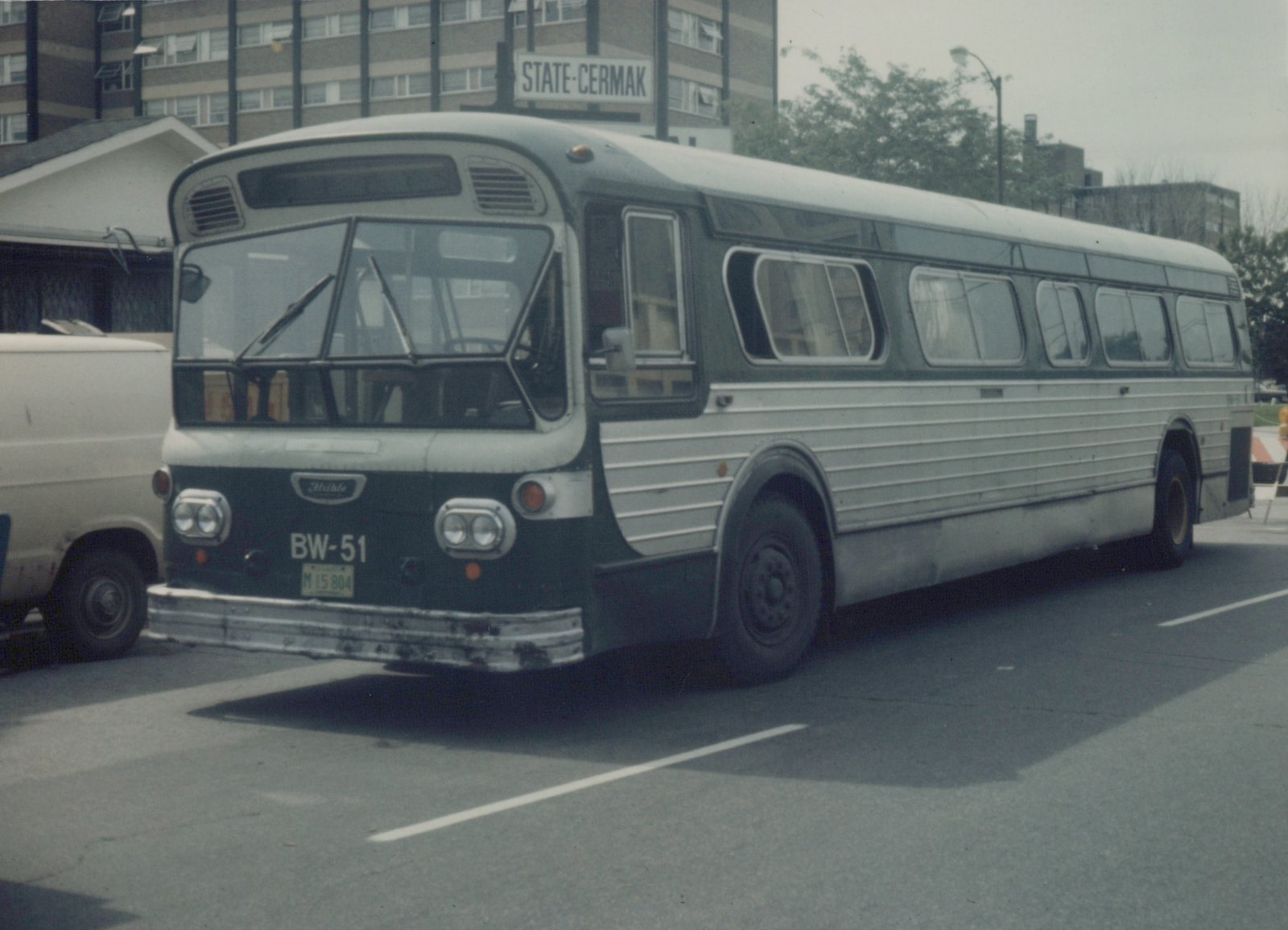 A vintage motor bus with a green and silver livery and the number BW-51 on its front, parked on an urban street with a sign reading 'STATE-CERMAK' in the background.
