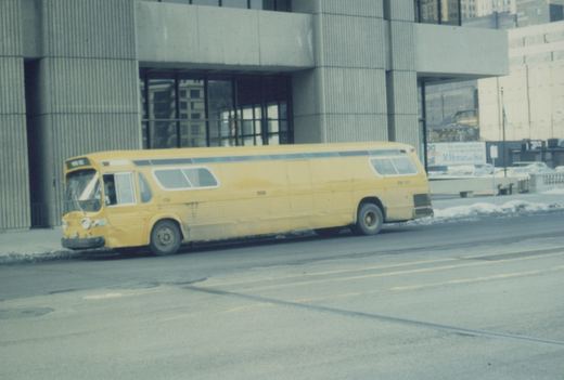 A side view of a yellow CTA bus parked on a snowy street next to a modern concrete building.
