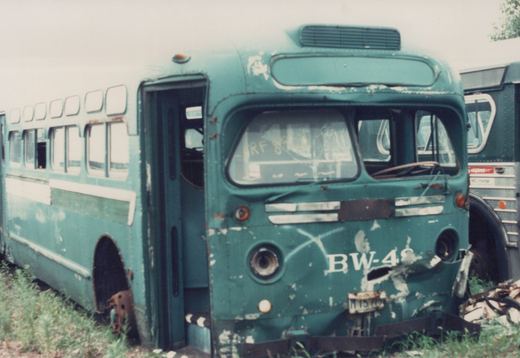 A green and white CTA bus with the number BW-48 on its front, showing signs of decay and missing wheels, parked in a grassy yard next to another bus.