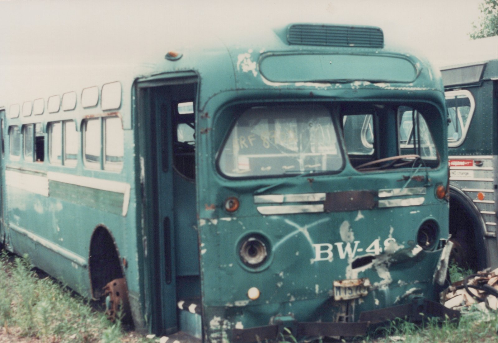 A green and white CTA bus with the number BW-48 on its front, showing signs of decay and missing wheels, parked in a grassy yard next to another bus.