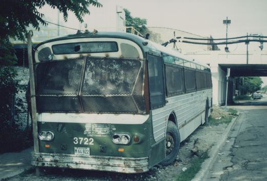 A worn green and white CTA motor bus, number 3722, with a mesh-covered front and an Illinois license plate, parked under a concrete overpass on a cloudy day.