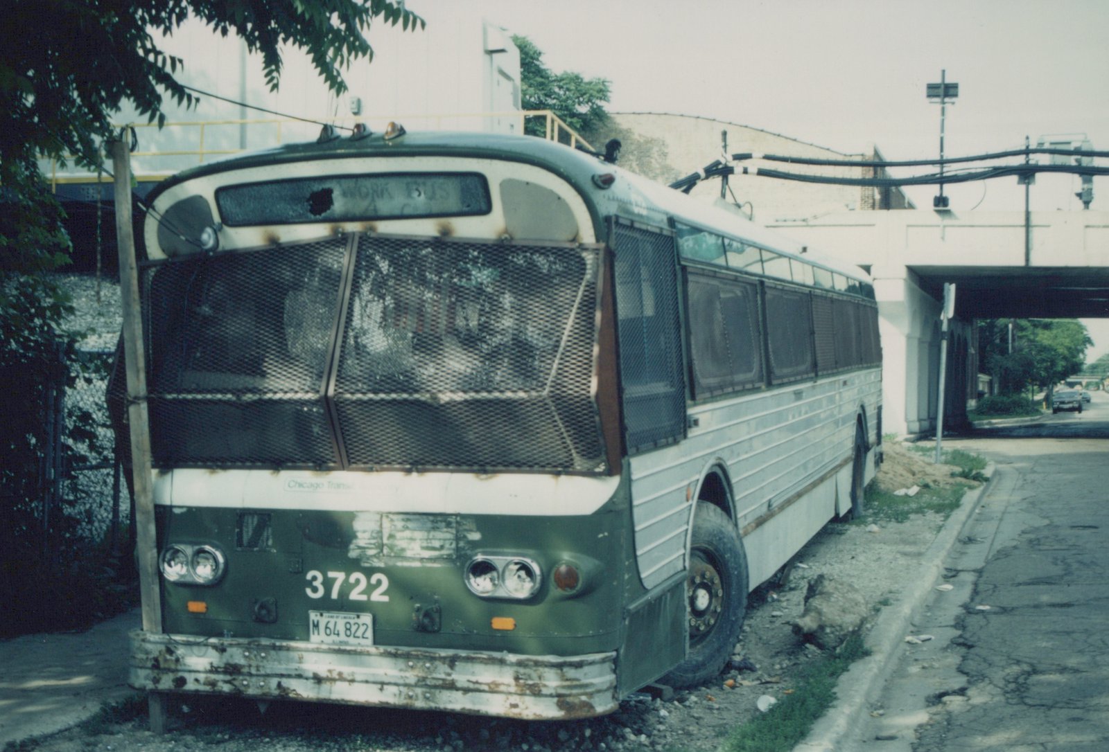 A worn green and white CTA motor bus, number 3722, with a mesh-covered front and an Illinois license plate, parked under a concrete overpass on a cloudy day.