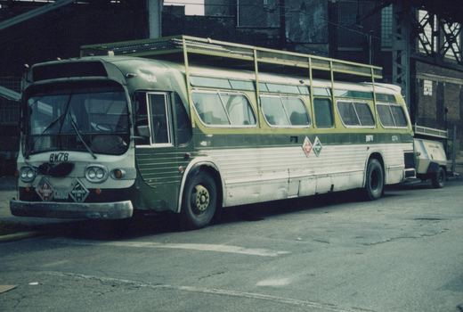 A green and white CTA bus, number BW78, is parked on a street with a small trailer attached to its rear. The bus has diamond-shaped hazard signs on its front bumper and a roof rack.