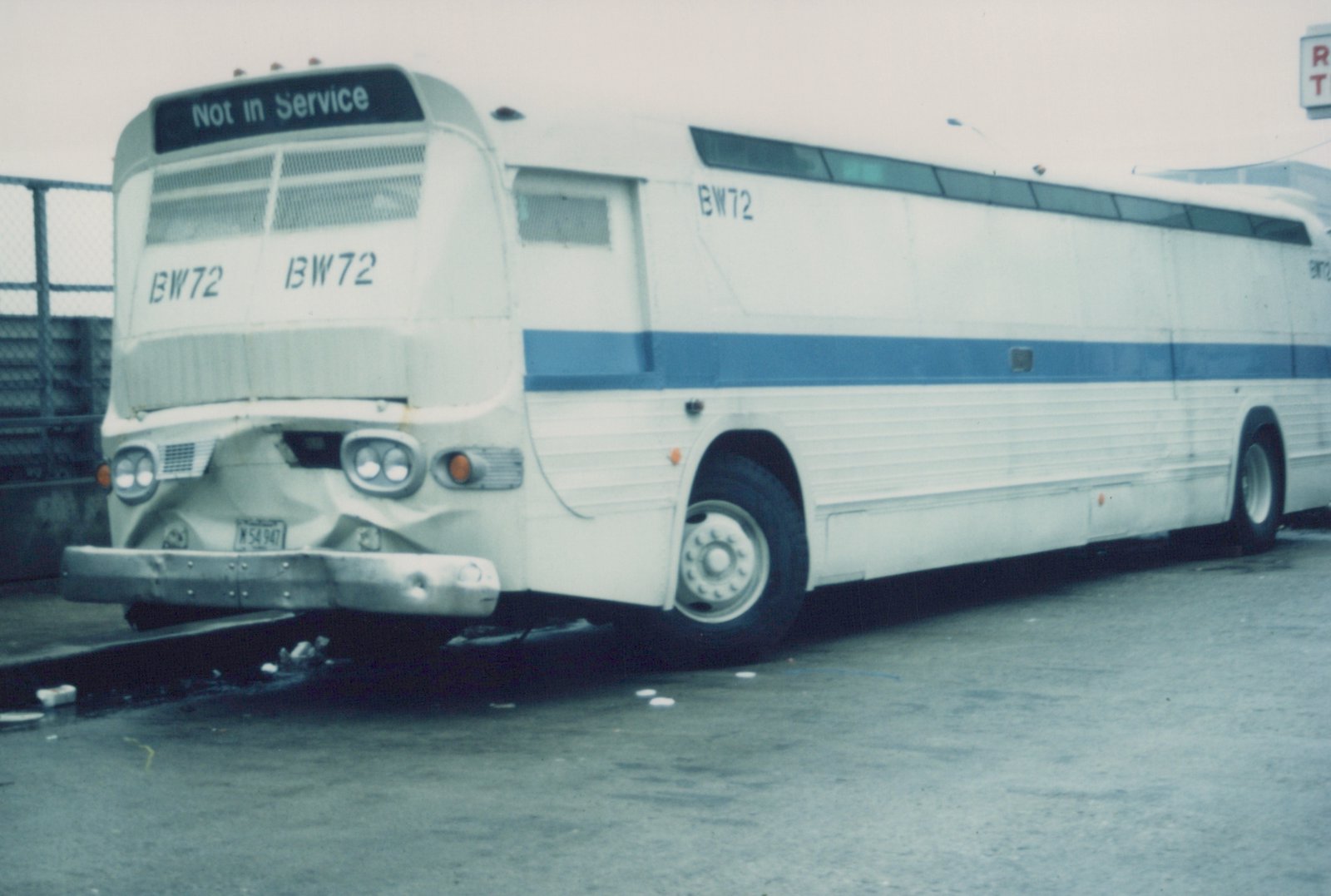 A white and blue motor bus with the number BW72 and 'Not in Service' on the front sign, parked in a paved lot. The front bumper is visibly damaged.