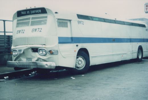A white and blue motor bus with the number BW72 and 'Not in Service' on the front sign, parked in a paved lot. The front bumper is visibly damaged.
