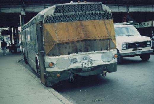 A front three-quarter view of a white and green Chicago Transit Authority bus with the number 1389, parked on a street under a bridge, next to a white van and near a food stand sign.