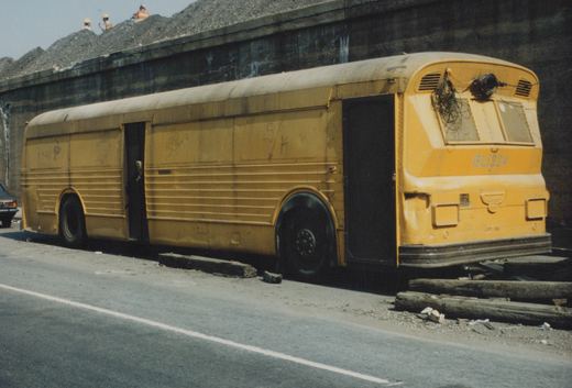 A yellow CTA New Look bus, number BL1324, is parked on the side of a street, with three people visible on a pile of gravel in the background.