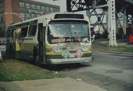 A white and green Chicago Transit Authority New Look bus, marked BW 79, is parked on a city street beneath a large steel bridge, with a brick building visible in the background.