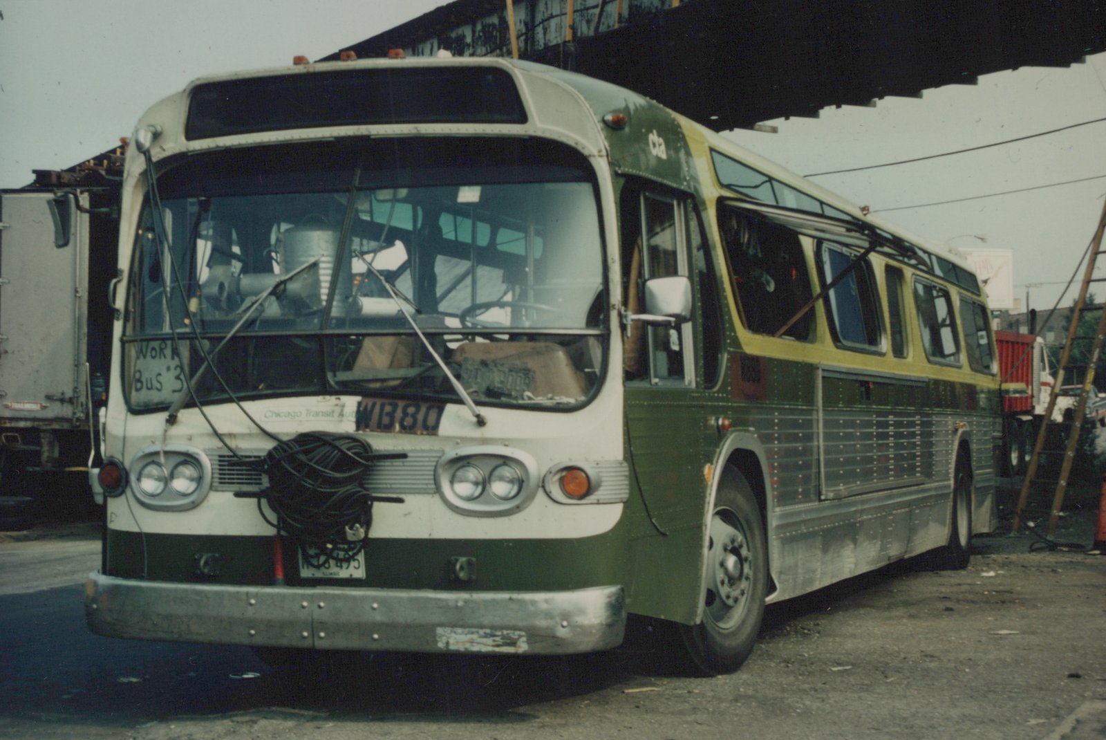 A green and cream Chicago Transit Authority motor bus, number WB80, is parked in a yard with its front facing the viewer; other trucks are visible in the background.