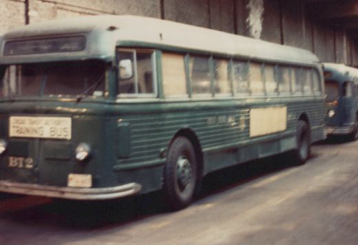 A green and white Chicago Transit Authority training bus, number BT2, is parked under a concrete underpass.