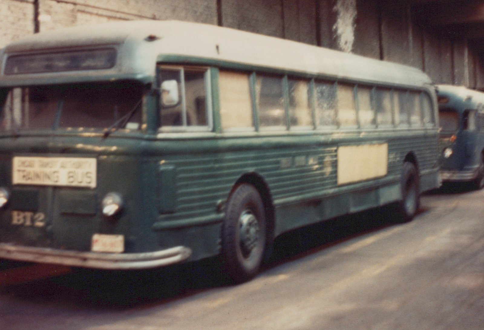 A green and white Chicago Transit Authority training bus, number BT2, is parked under a concrete underpass.