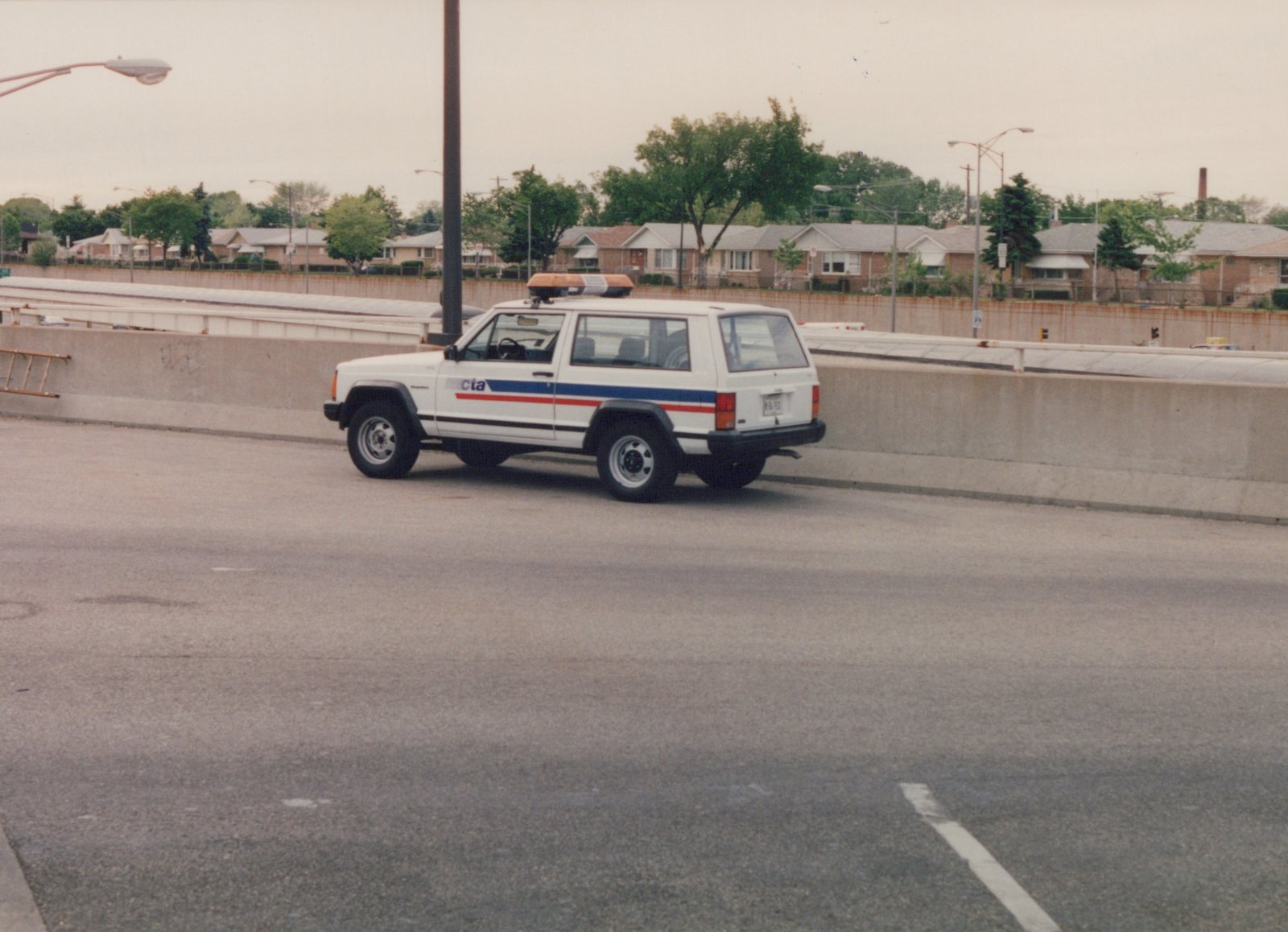A white Chicago Transit Authority Jeep Cherokee utility vehicle with red and blue stripes, viewed from the rear three-quarter angle on a concrete highway median.