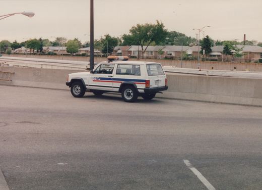 A white Chicago Transit Authority Jeep Cherokee utility vehicle with red and blue stripes, viewed from the rear three-quarter angle on a concrete highway median.