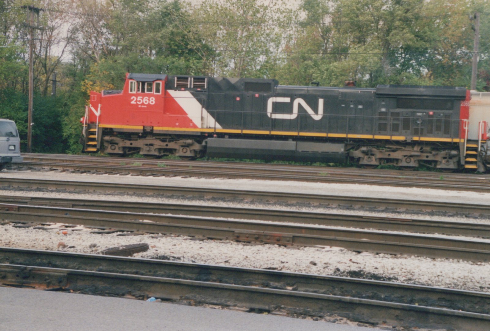 Side view of a red, white and black Canadian National diesel locomotive numbered 2568, with a white CN logo on its black hood, parked beyond several sets of yard tracks with trees behind.