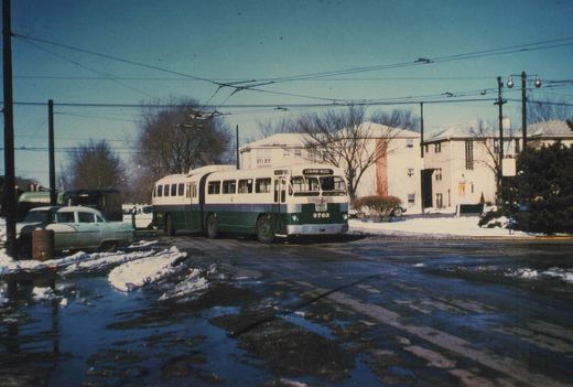 A green and cream Chicago Transit Authority trolleybus, number 9763, on route 11 Belmont-Halsted, is parked on a snow-covered street with bare trees and apartment buildings in the background.