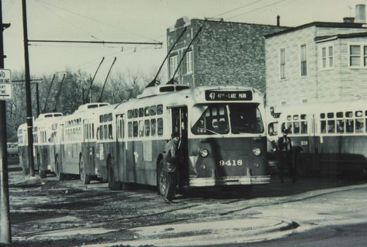 A black and white photo shows a CTA trolleybus with the number 9418 and route 47 to Lake Park, stopped on a street with a trolley pole raised, with another CTA bus nearby and a person boarding.