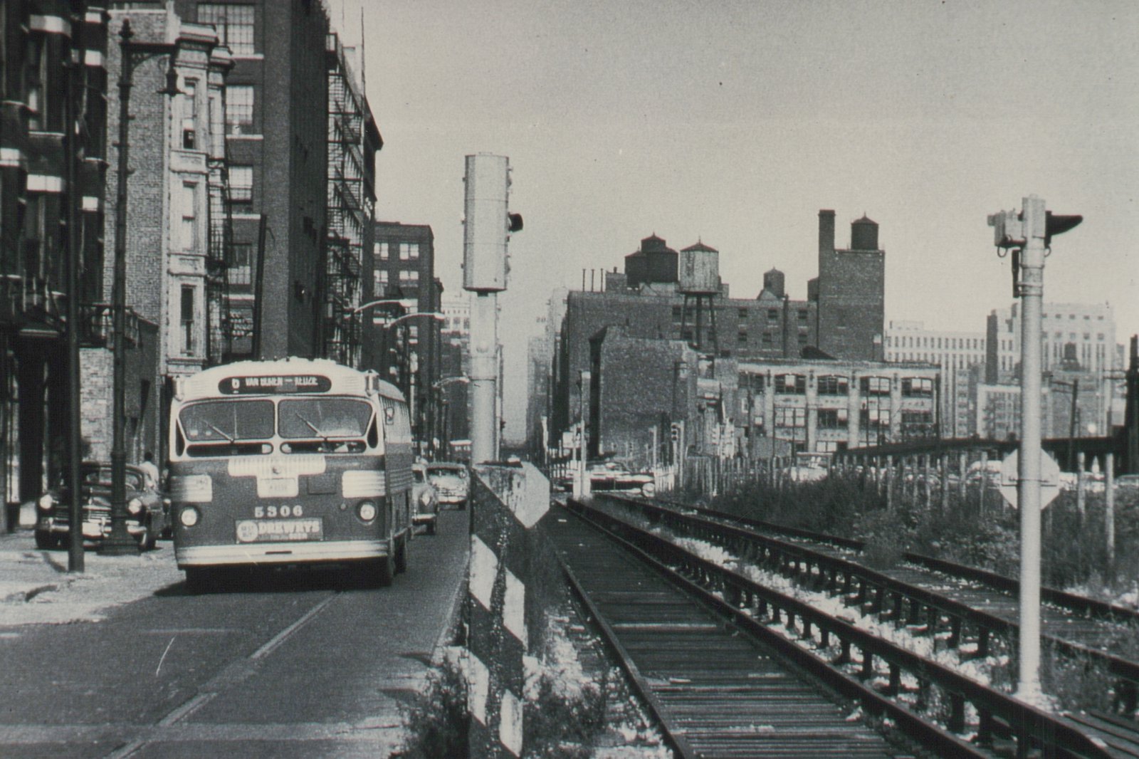 Front view of a dark-bodied CTA bus with the number 5306 and a 'Van Buren - Racine' destination sign, driving on a snowy city street next to elevated train tracks.