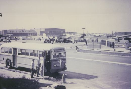 A 1940s motor bus from Chicago Surface Lines, fleet number 318, labeled 'Archer Express Cicero-63', is stopped at a bus stop on a sunny day, with American Airlines and Texaco buildings visible in the background.