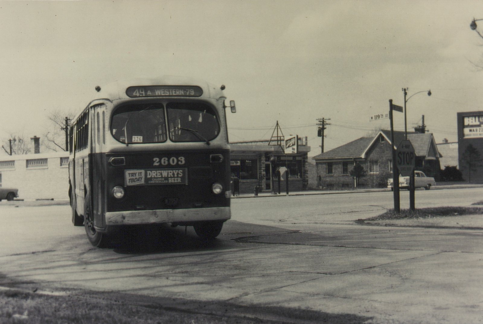 A black and white photo of a Chicago Transit Authority bus turning at a street intersection with a stop sign and a street sign for 119th Street visible.