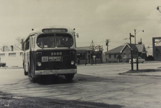 A black and white photo of a Chicago Transit Authority bus turning at a street intersection with a stop sign and a street sign for 119th Street visible.