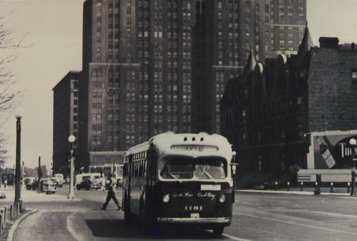 A black and white photo of a 1950s GMC New Look bus with the number 1181 and destination 'UNIVERSITY' on a city street with pedestrians and tall buildings in the background.
