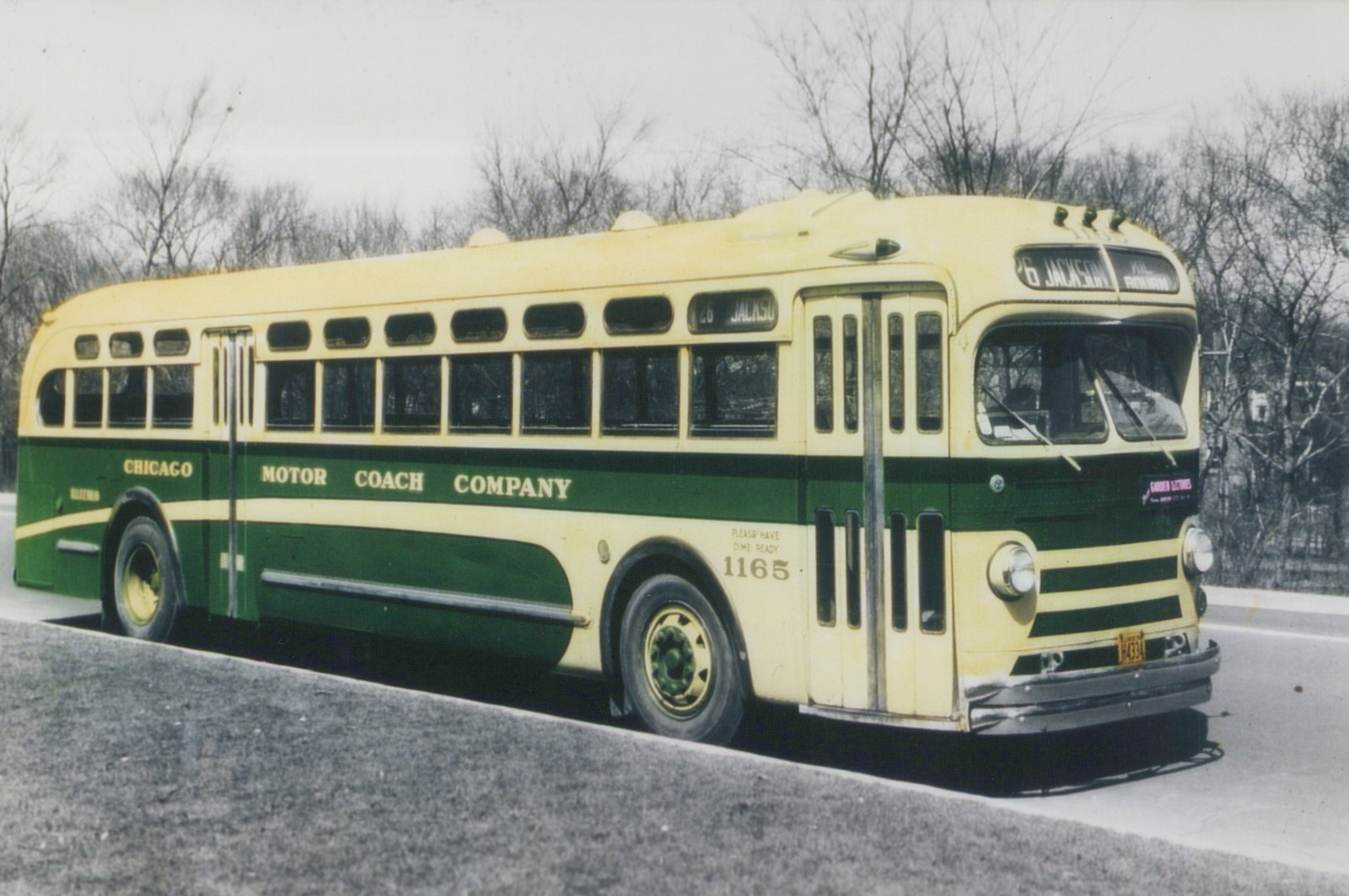A vintage green and cream Chicago Motor Coach Company bus, number 1165, is parked on a street with bare trees in the background. The destination sign reads '26 Jackson Via Harmon'.