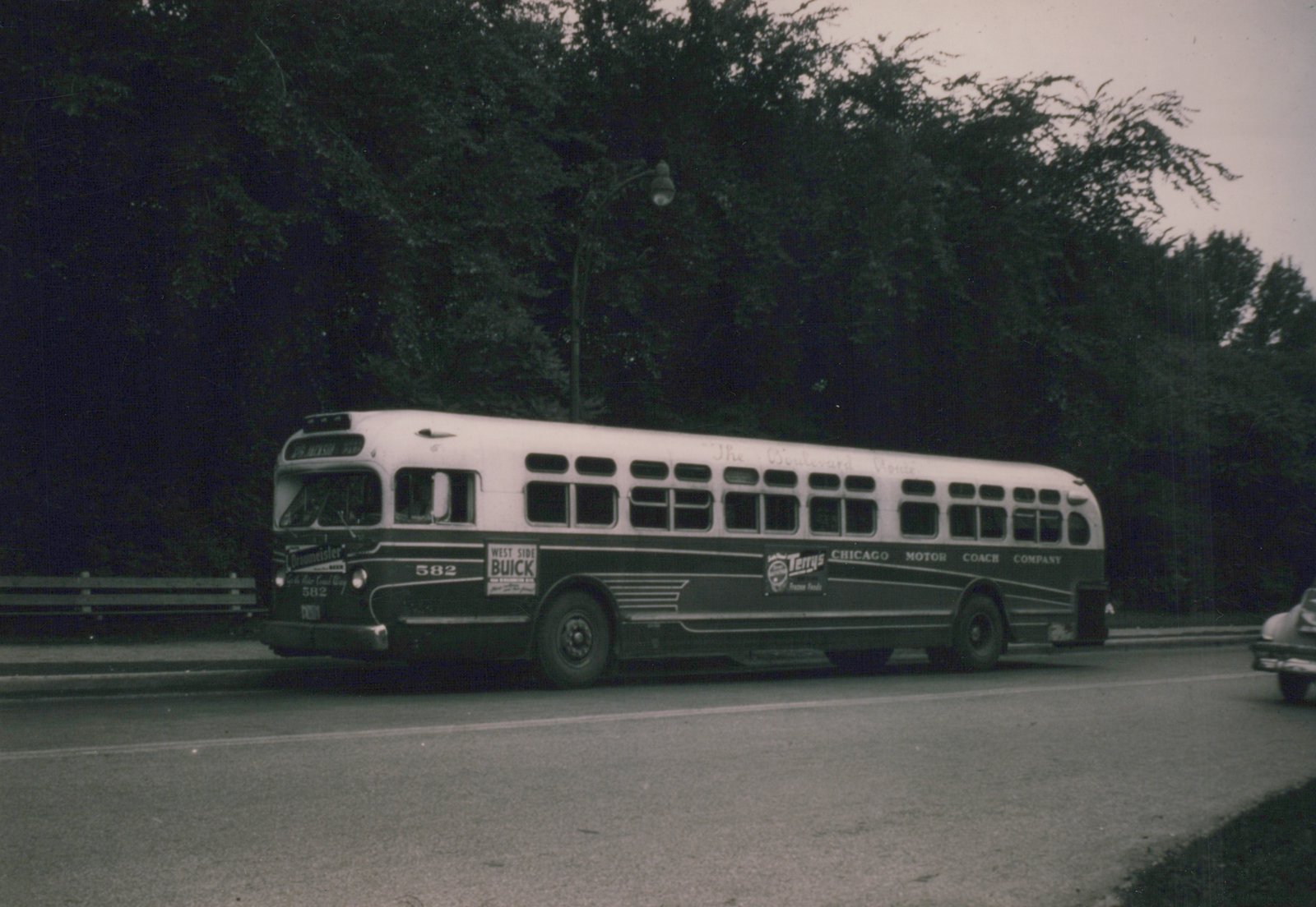 A vintage motor bus with number 582 and Chicago Motor Coach Company lettering is driving down a tree-lined street.