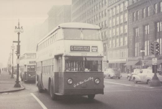 A vintage black-and-white photograph of a double-decker bus with the number 212 on a city street, with other buses and cars in the background.