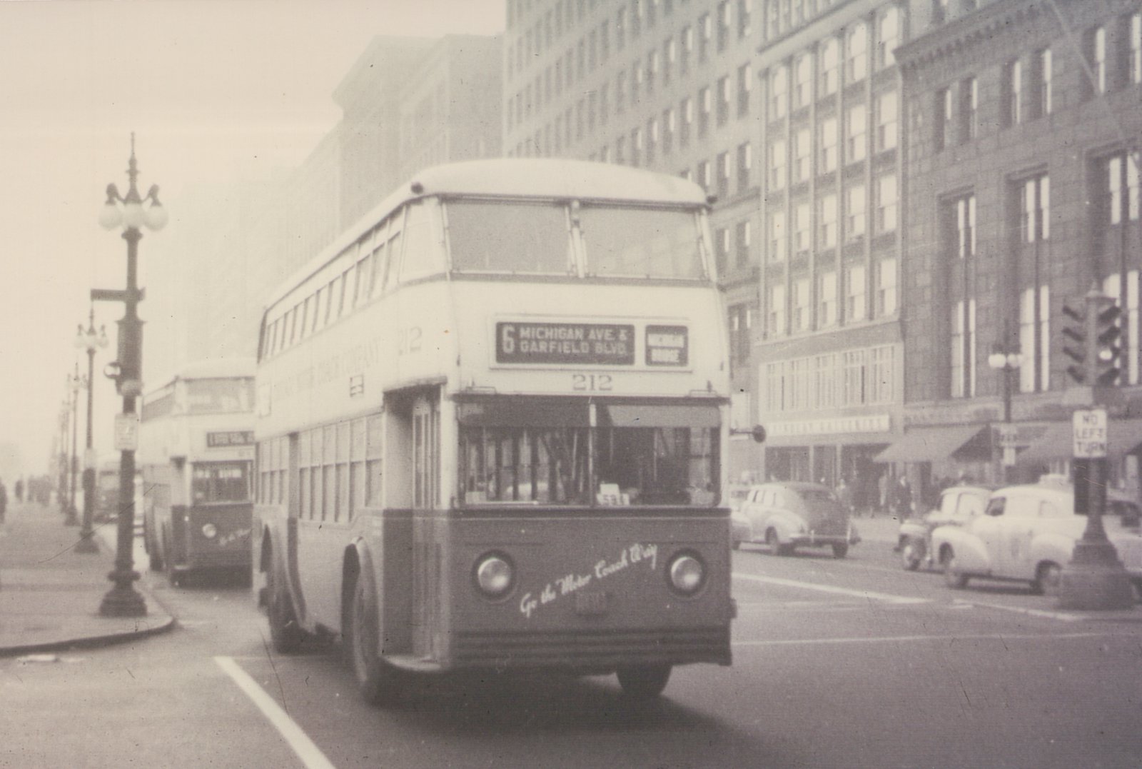 A vintage black-and-white photograph of a double-decker bus with the number 212 on a city street, with other buses and cars in the background.