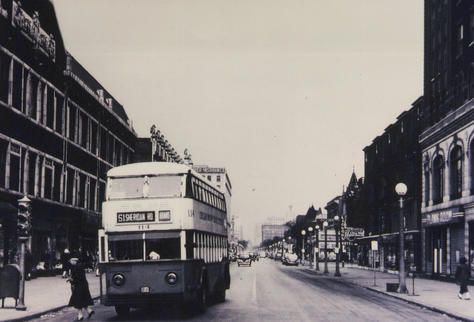 A black-and-white photo shows a vintage double-decker bus on a wide city street, with pedestrians on the sidewalks and multi-story buildings lining the road. The bus displays route 51 Sheridan Road and destination Adams.