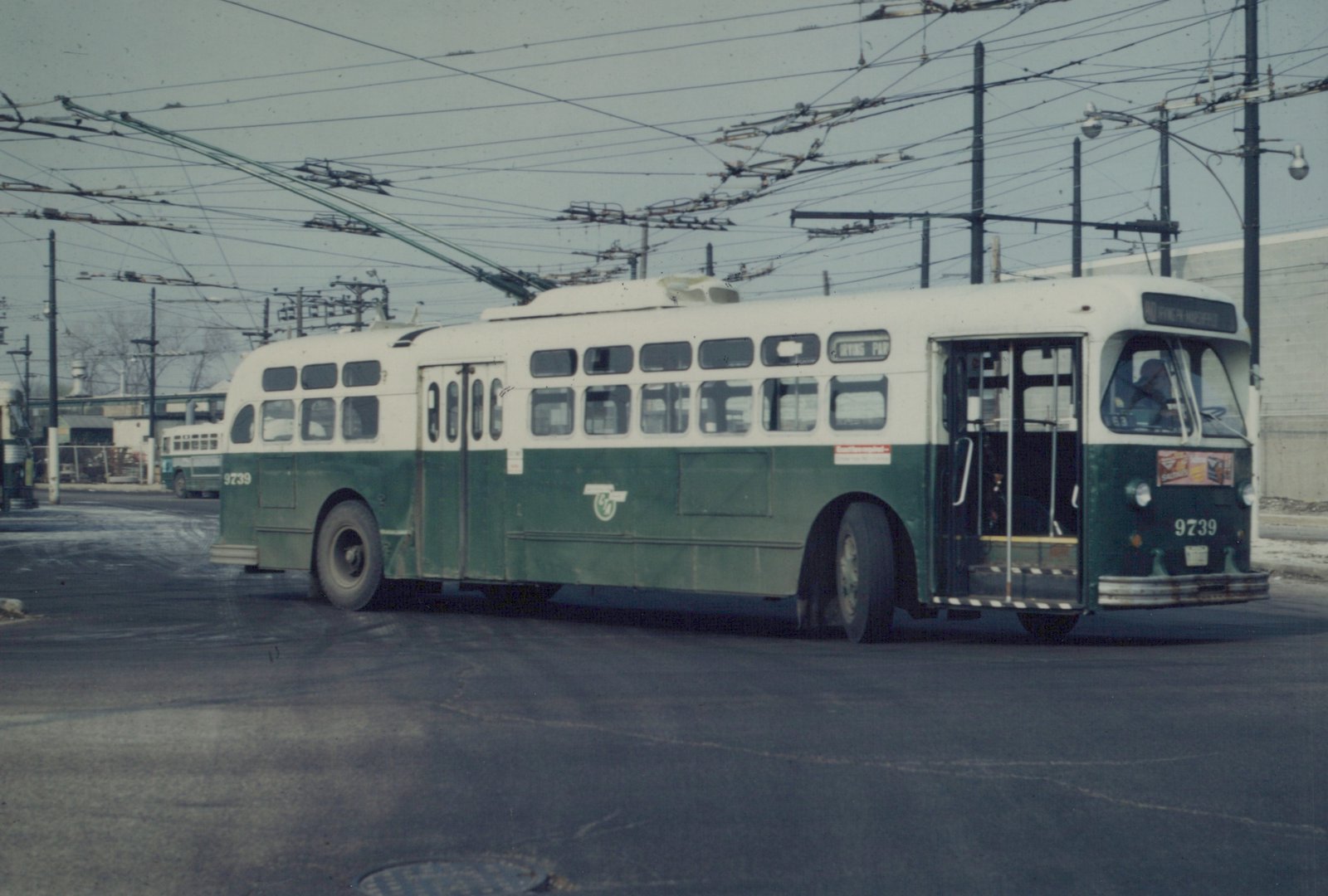 A green and cream CTA trolleybus numbered 9739, showing its destination as Irving Park, parked on a wet street under a web of trolley wires.
