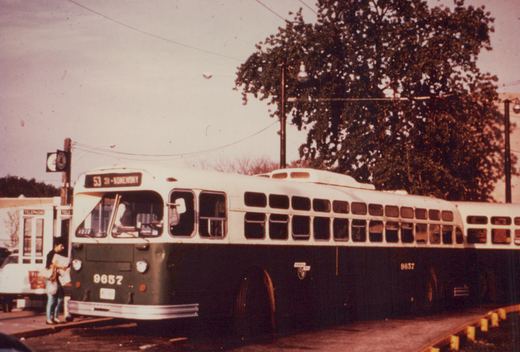A white and green Chicago Transit Authority bus, number 9657, is stopped at a curb with passengers nearby, under an overcast sky with autumn trees in the background.