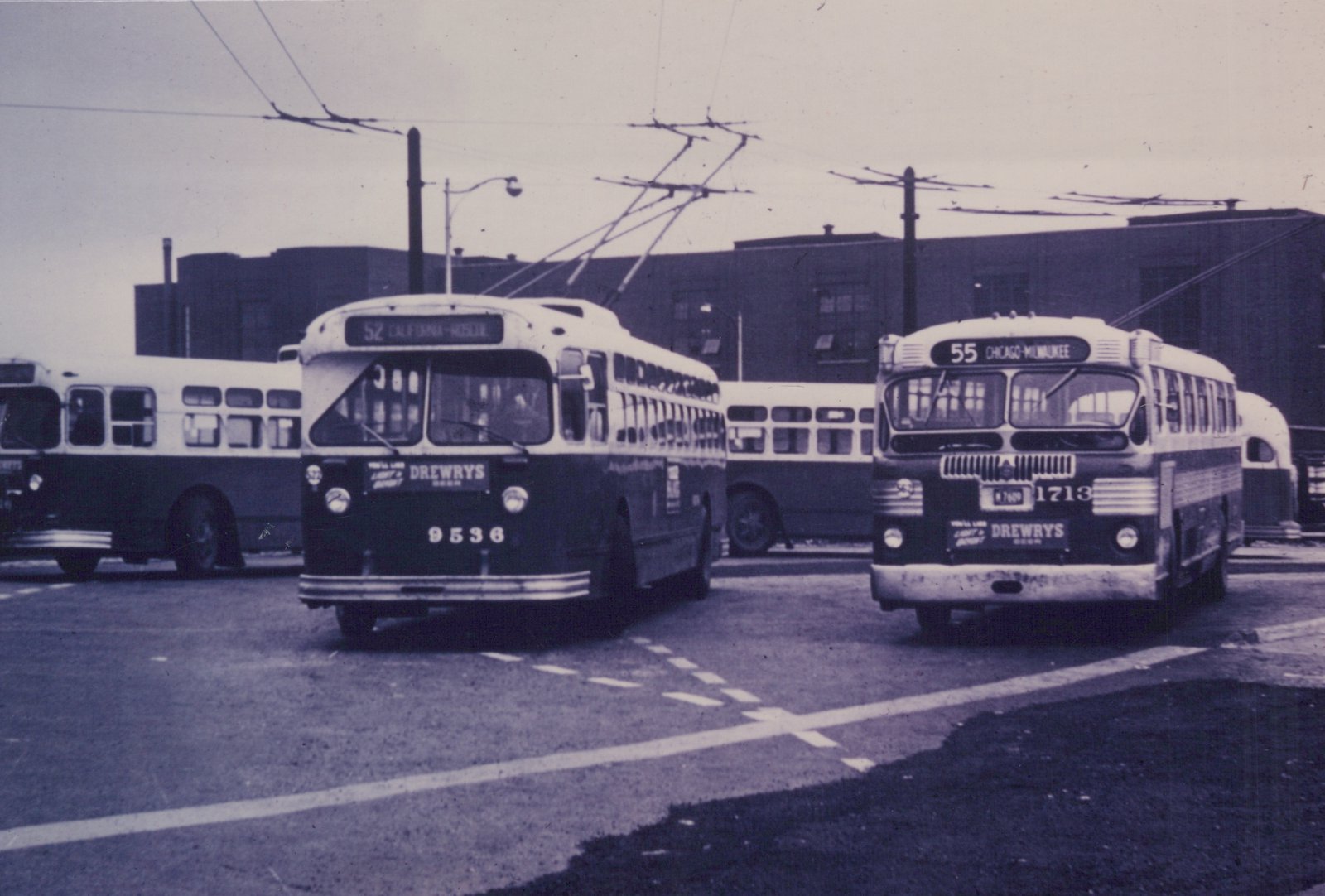 A black and white photo of two vintage buses from Drewry's, numbered 9536 and 1713, parked on a street under trolley wires. One shows route 52 to California-Roscoe, the other route 55 to Chicago-Milwaukee.