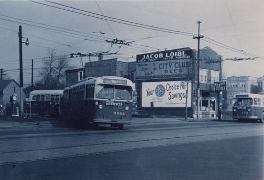 A black and white photo of a Chicago Transit Authority trolleybus, number 9563, on route 86 NARRAGANSETT, driving down a street with overhead wires and a building displaying ads for Jacob Loibl and City Club Beer.