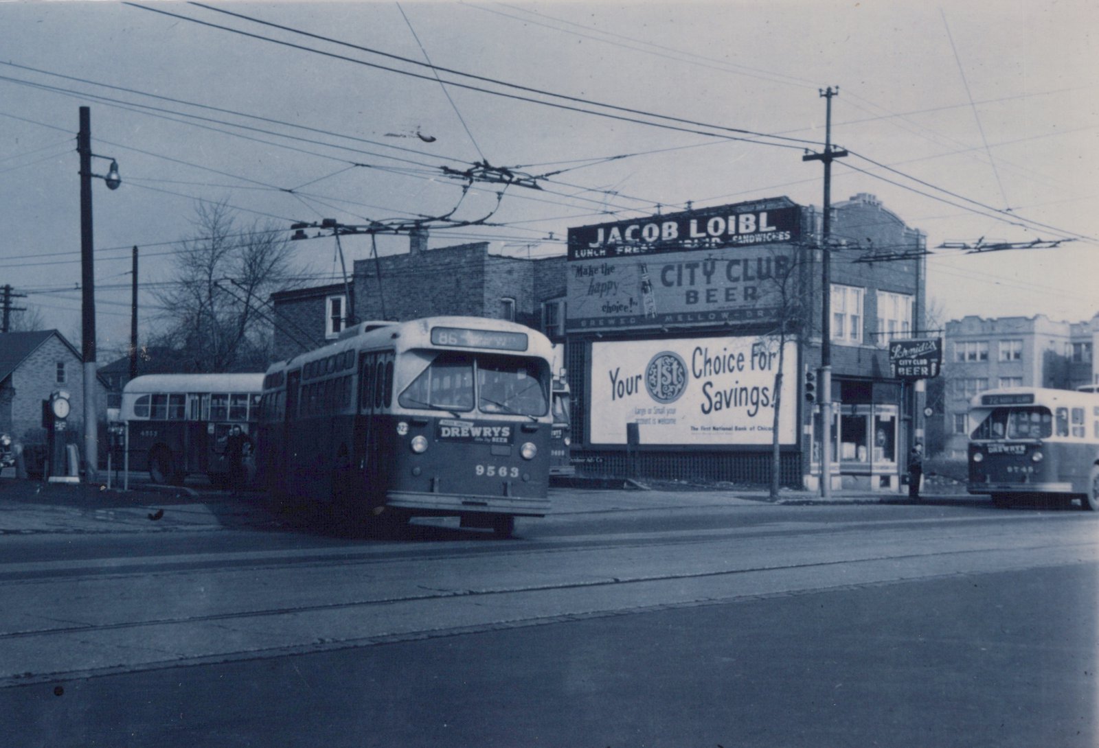 A black and white photo of a Chicago Transit Authority trolleybus, number 9563, on route 86 NARRAGANSETT, driving down a street with overhead wires and a building displaying ads for Jacob Loibl and City Club Beer.