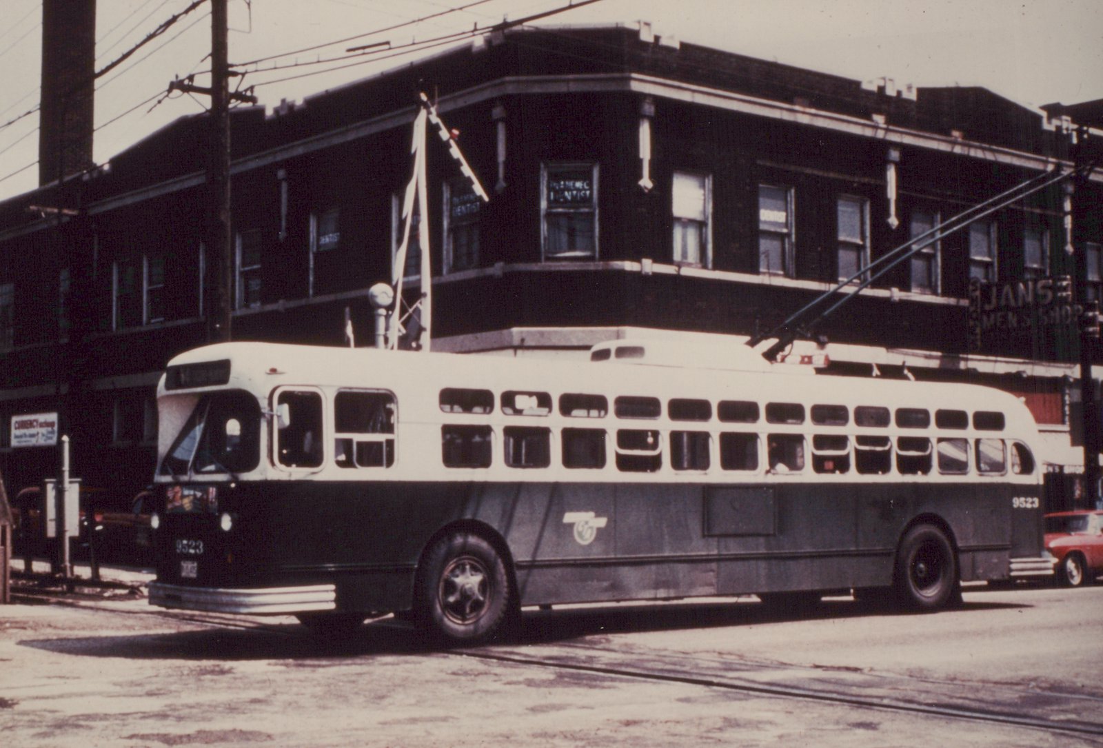 A black and white photo of a Chicago Transit Authority trolleybus, number 9523, parked on a street with overhead wires and buildings in the background.