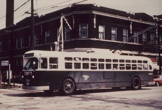 A black and white photo of a Chicago Transit Authority trolleybus, number 9523, parked on a street with overhead wires and buildings in the background.
