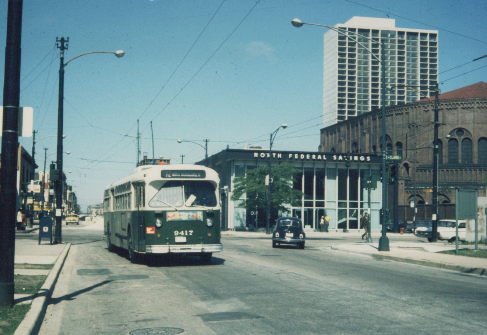 A green and cream trolleybus numbered 9417 travels down a city street under overhead wires, with a modern building labeled 'NORTH FEDERAL SAVINGS' and a 'CLARK' street sign visible, alongside vintage automobiles and pedestrians.