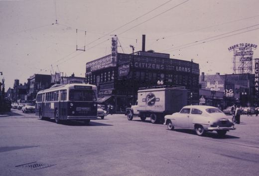 A vintage trolleybus travels down a busy street in Chicago, with storefronts like Citizens Loan Corp and a Fred Astaire dance studio sign in the background.