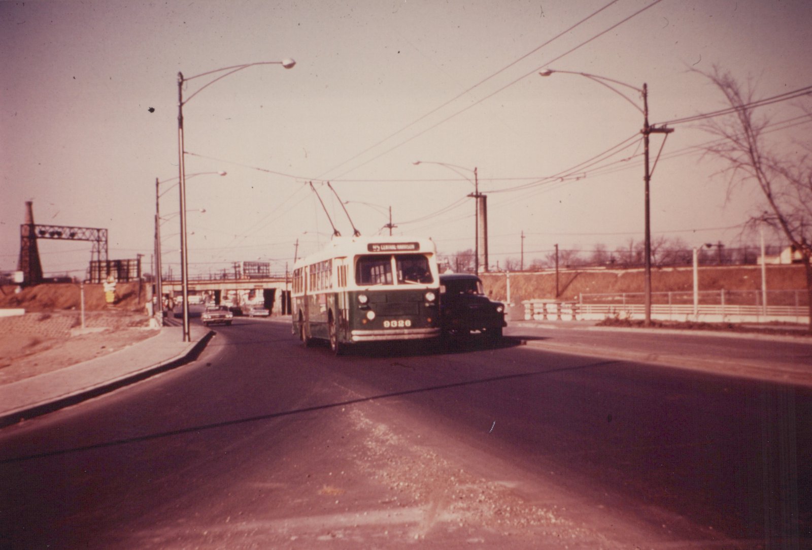 A green and cream Chicago Transit Authority trolleybus, number 9326, is driving on a street with overhead wires, with a truck beside it and an overpass in the background.