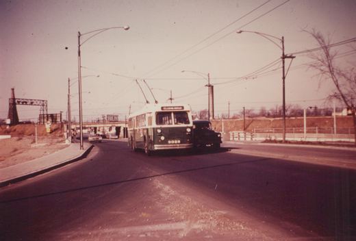 A green and cream Chicago Transit Authority trolleybus, number 9326, is driving on a street with overhead wires, with a truck beside it and an overpass in the background.